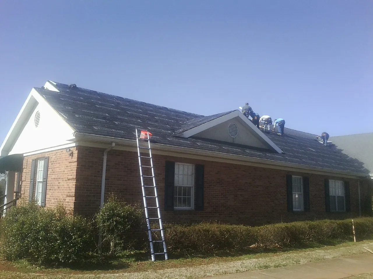 Crew tearing shingles off a brick ranch roof with a ladder set — Metal Roof Repair work by our crew in Mosinee