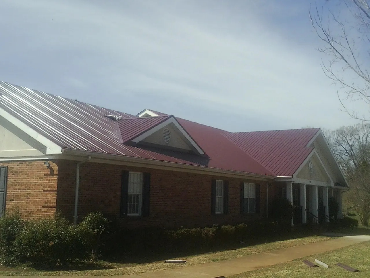 Red metal roof with gabled entries on a long brick building, from a Hail Damage Roof Repair job in Mosinee