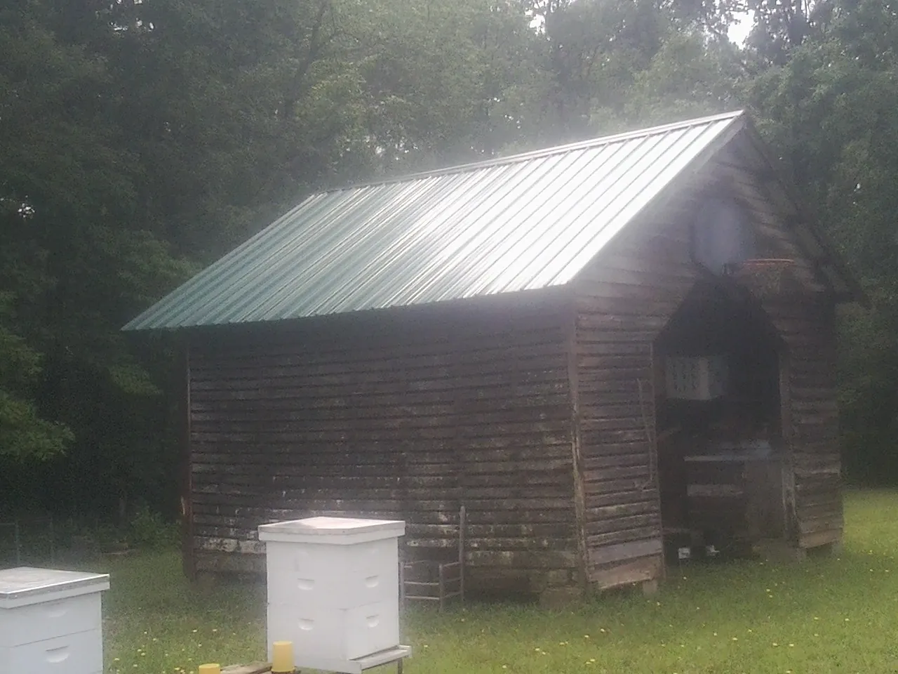 Green metal roof on a weathered barn beside stacked beehives in Mosinee