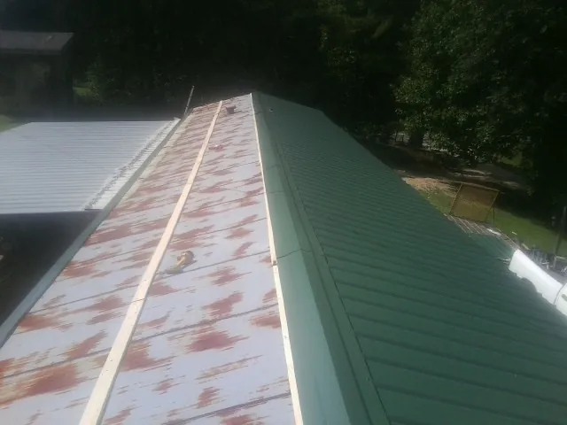 Old rusted panels beside newly installed green metal roofing — Wind Damage Roof Repair by Roofing Brothers in Mosinee