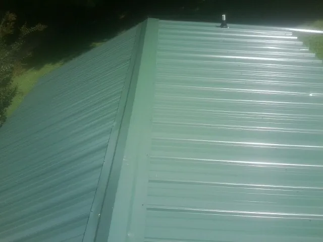 New green metal panels meeting at the ridge of a roof — Flat Roof Repair work by our crew in Mosinee