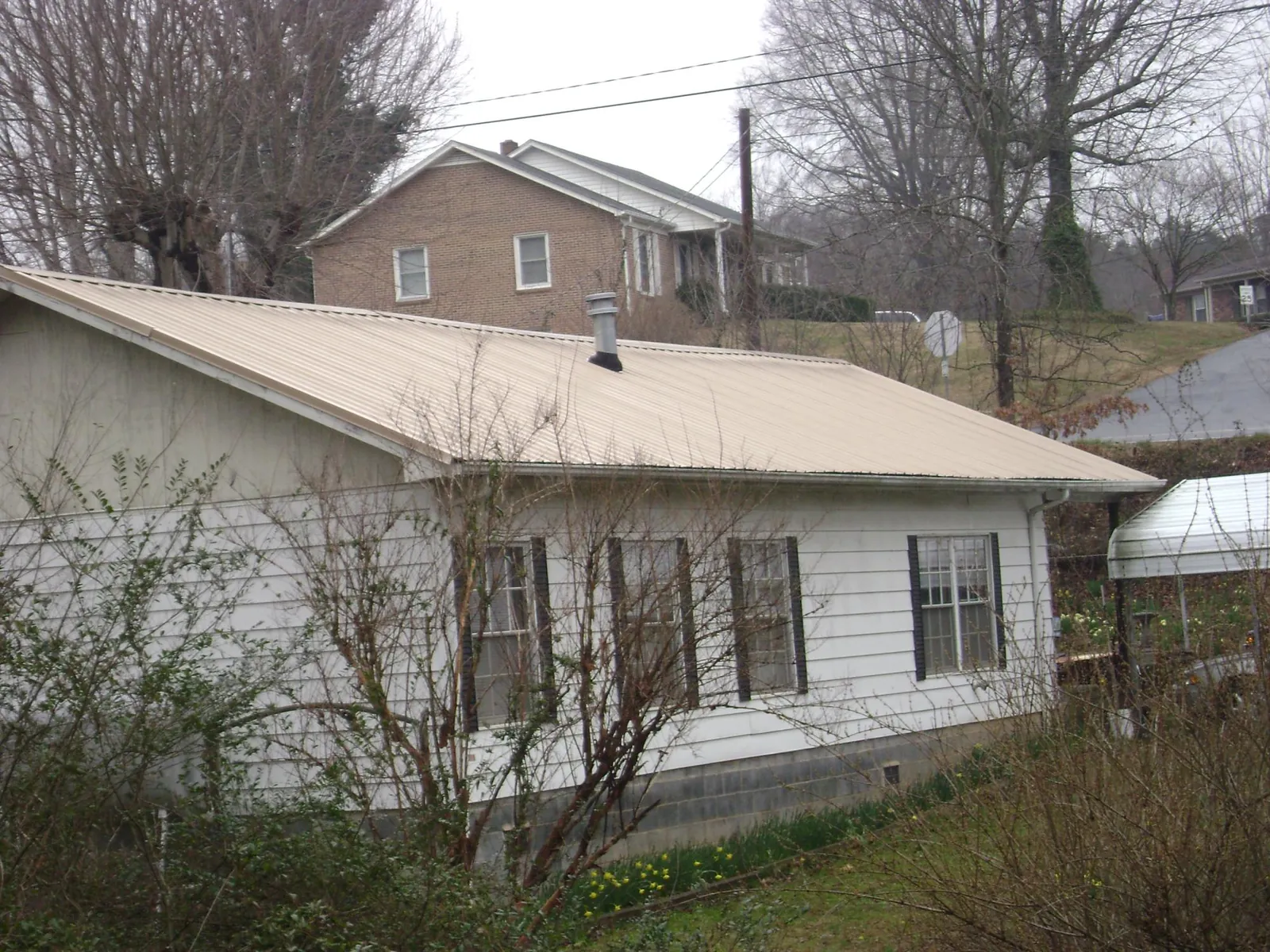 Tan metal roof on a white sided house set into a hillside — Commercial Roofing by Roofing Brothers in Mosinee
