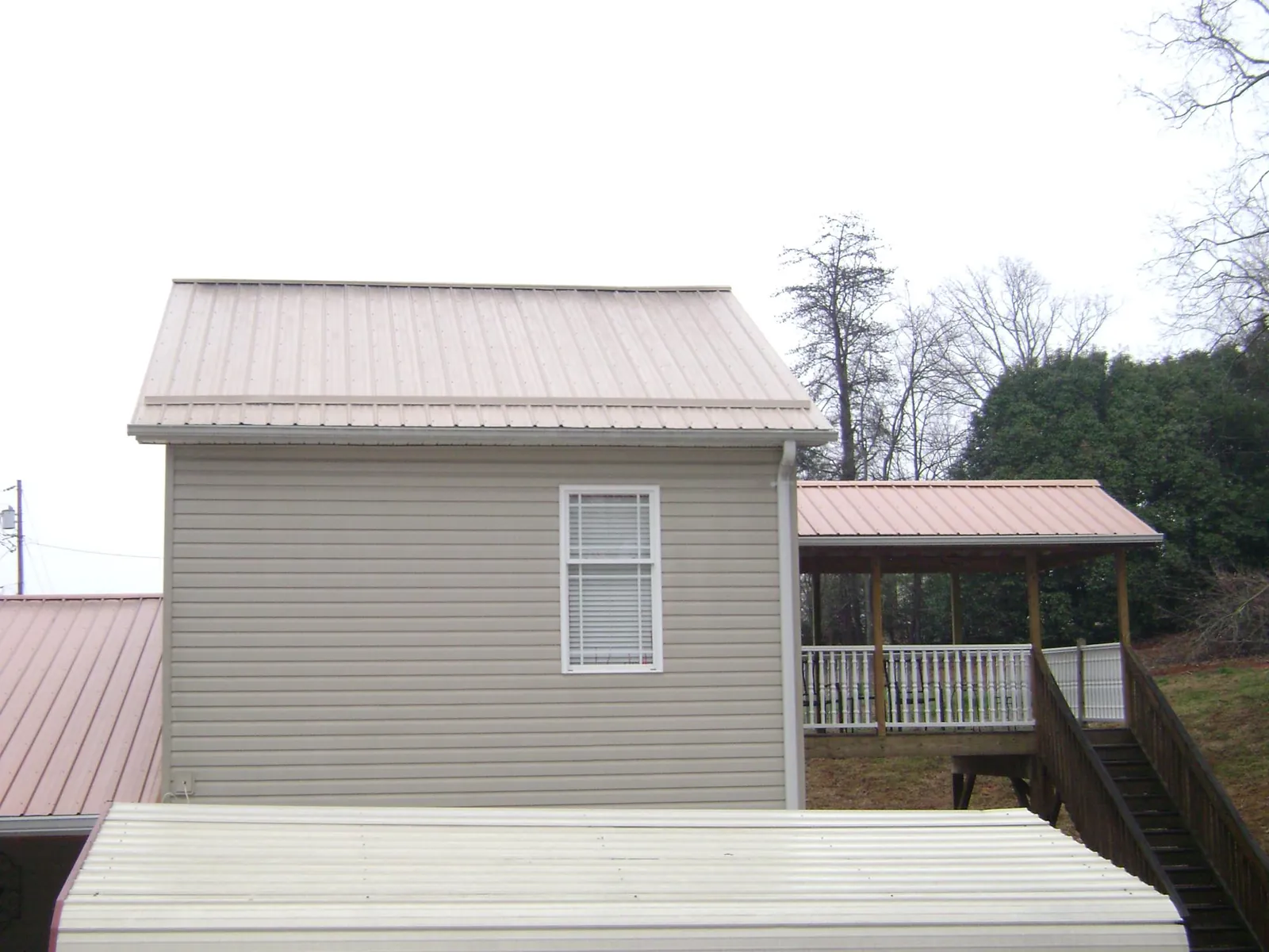 Tan metal roofs on a two story addition and attached porch, from a Roof Replacement job in Mosinee